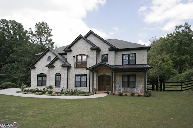 view of front facade with a balcony, fence, a front lawn, and brick siding