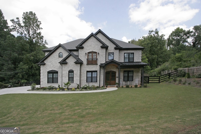 french country home with a front lawn, a standing seam roof, fence, and brick siding