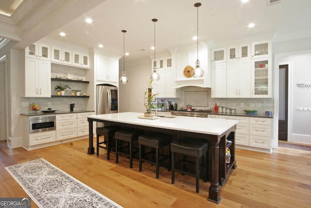 kitchen with a breakfast bar area, a kitchen island with sink, stainless steel refrigerator with ice dispenser, light wood-type flooring, and open shelves