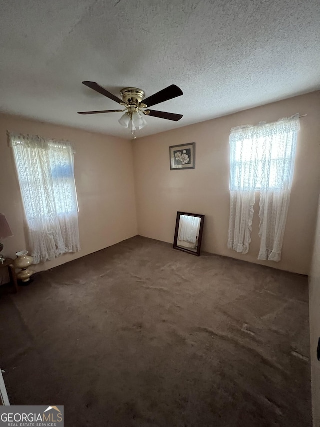 carpeted spare room with a textured ceiling, ceiling fan, and plenty of natural light