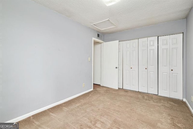 unfurnished bedroom with visible vents, a textured ceiling, carpet, baseboards, and attic access