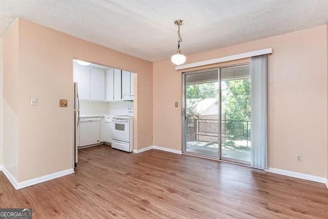 unfurnished dining area with baseboards, a textured ceiling, and light wood-style flooring