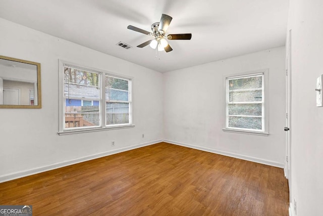 spare room featuring a healthy amount of sunlight, ceiling fan, baseboards, and wood finished floors