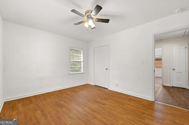 unfurnished bedroom with attic access, wood finished floors, a ceiling fan, and baseboards