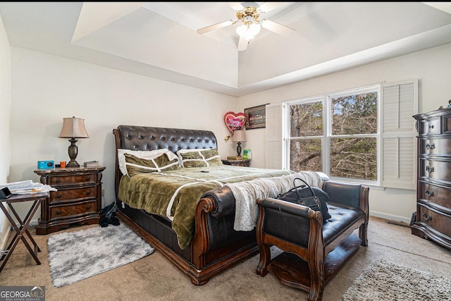 carpeted bedroom featuring a tray ceiling, ceiling fan, and baseboards