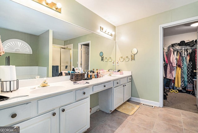 bathroom featuring a sink, baseboards, a shower stall, double vanity, and a walk in closet