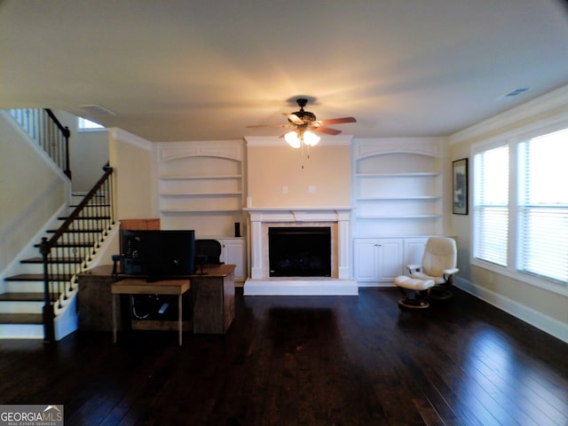 living room featuring baseboards, built in features, hardwood / wood-style flooring, ornamental molding, and a fireplace