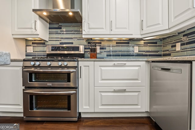 kitchen with stainless steel appliances, white cabinets, backsplash, wall chimney exhaust hood, and dark wood finished floors