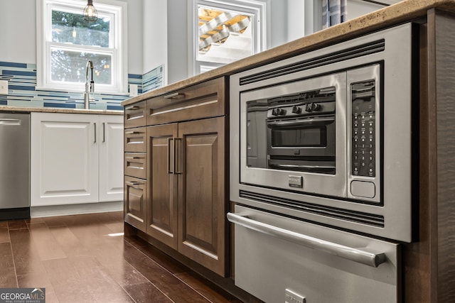 kitchen featuring a warming drawer, backsplash, appliances with stainless steel finishes, white cabinets, and a sink