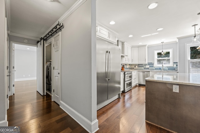 kitchen with a barn door, appliances with stainless steel finishes, tasteful backsplash, and crown molding