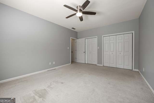 unfurnished bedroom with baseboards, visible vents, ceiling fan, carpet floors, and two closets