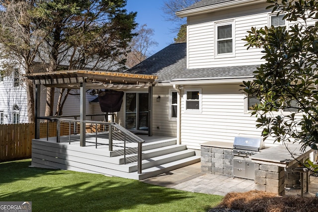 back of property featuring an outdoor kitchen, fence, roof with shingles, a wooden deck, and a pergola