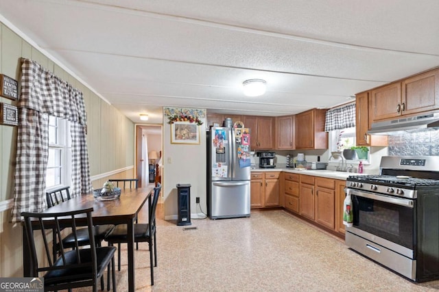 kitchen featuring brown cabinets, stainless steel appliances, light countertops, a sink, and under cabinet range hood