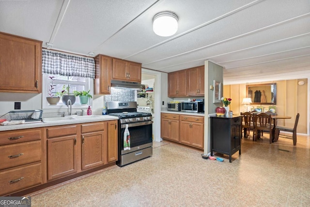 kitchen with light floors, stainless steel appliances, light countertops, a sink, and under cabinet range hood