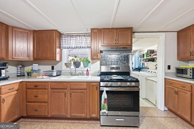 kitchen featuring brown cabinets, light countertops, washing machine and dryer, under cabinet range hood, and stainless steel gas range oven