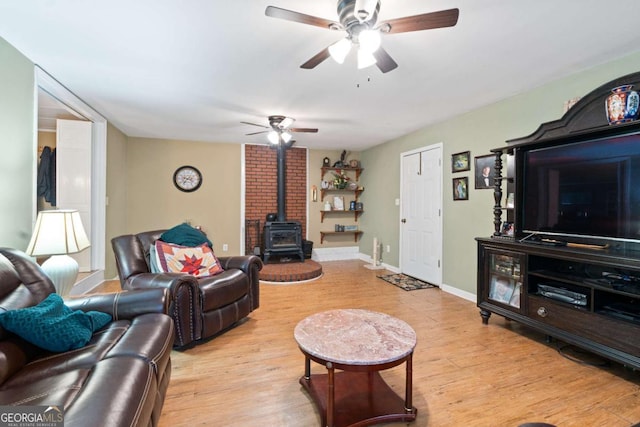 living room featuring ceiling fan, light wood-style flooring, a wood stove, and baseboards