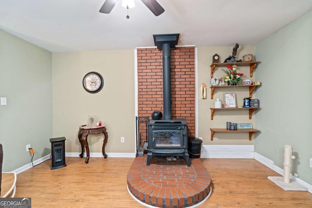 living area with a wood stove, light wood finished floors, ceiling fan, and baseboards