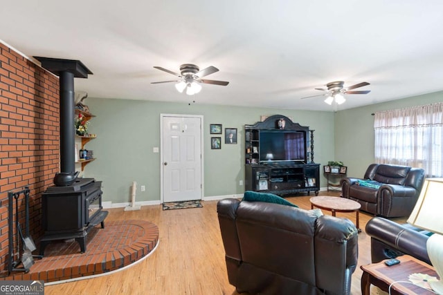 living area with a wood stove, baseboards, a ceiling fan, and wood finished floors