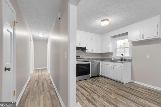 kitchen featuring light wood-type flooring, under cabinet range hood, white cabinetry, and appliances with stainless steel finishes