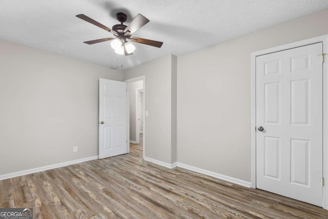 unfurnished bedroom featuring baseboards, ceiling fan, a textured ceiling, and light wood-style floors