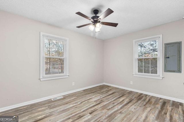 unfurnished room featuring a wealth of natural light, wood finished floors, visible vents, and baseboards