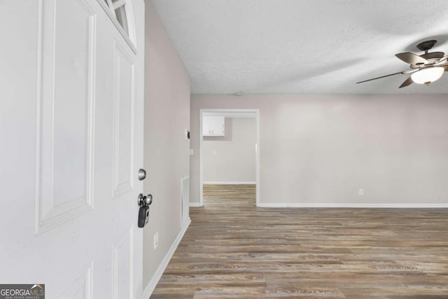 empty room with ceiling fan, a textured ceiling, baseboards, and wood finished floors