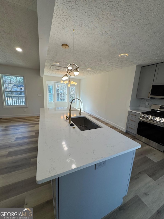 kitchen featuring light stone counters, wood finished floors, a sink, appliances with stainless steel finishes, and gray cabinets