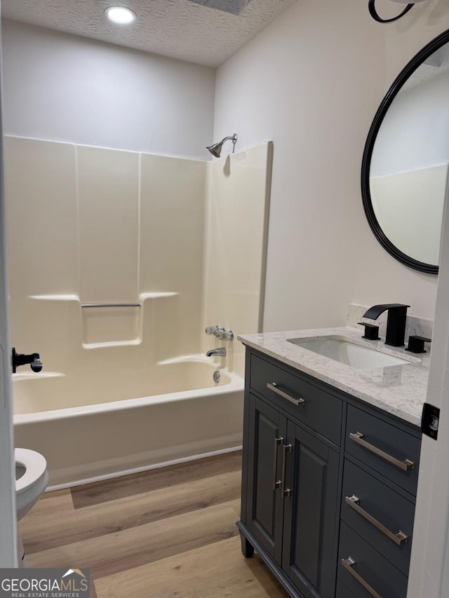 full bath with toilet, a textured ceiling, vanity, wood finished floors, and  shower combination