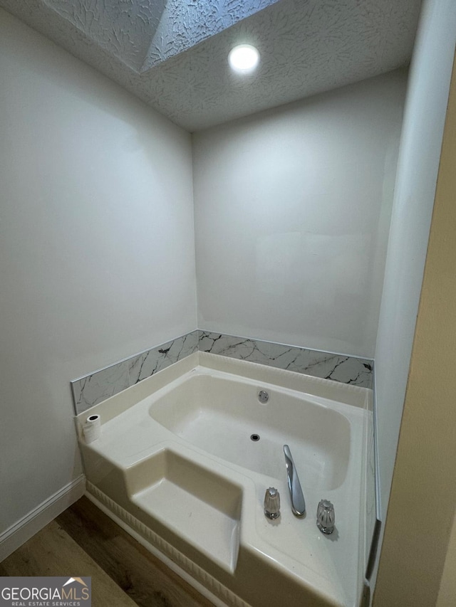 bathroom with a textured ceiling, wood finished floors, a bath, and baseboards