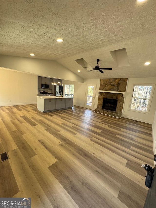 unfurnished living room with lofted ceiling, visible vents, a fireplace, and light wood finished floors