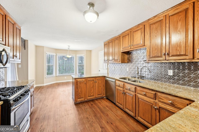 kitchen featuring brown cabinetry, decorative light fixtures, a peninsula, stainless steel appliances, and a sink