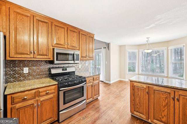 kitchen featuring light stone counters, hanging light fixtures, backsplash, appliances with stainless steel finishes, and brown cabinetry