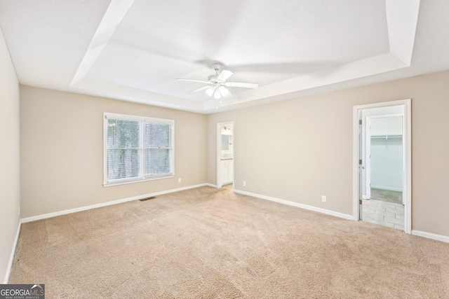 unfurnished room featuring a raised ceiling, visible vents, light carpet, ceiling fan, and baseboards