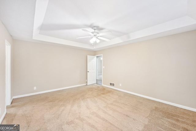 unfurnished room with ceiling fan, light colored carpet, visible vents, baseboards, and a raised ceiling