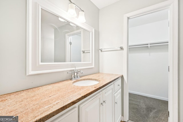 bathroom with a walk in closet, vanity, and baseboards