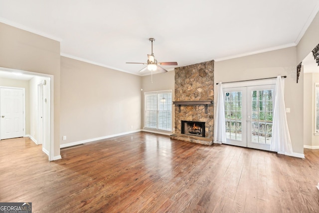 unfurnished living room featuring crown molding, a ceiling fan, a stone fireplace, wood finished floors, and baseboards