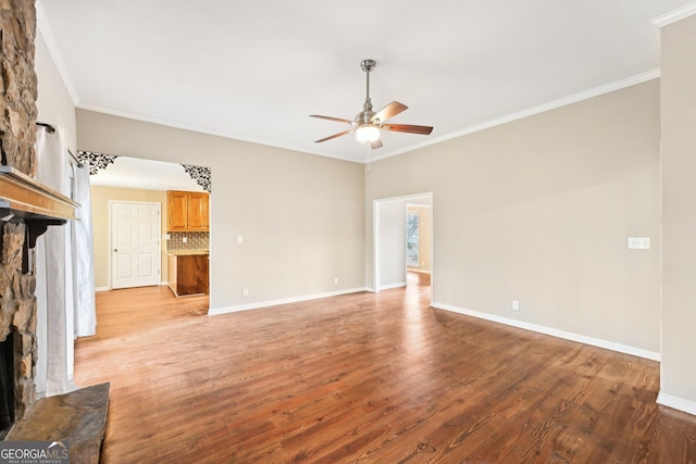 unfurnished living room with crown molding, light wood-style floors, ceiling fan, a stone fireplace, and baseboards