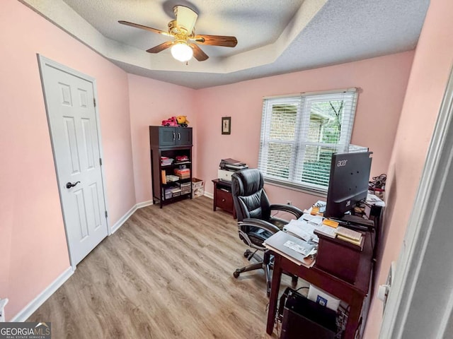 office area featuring baseboards, a raised ceiling, ceiling fan, a textured ceiling, and light wood-type flooring