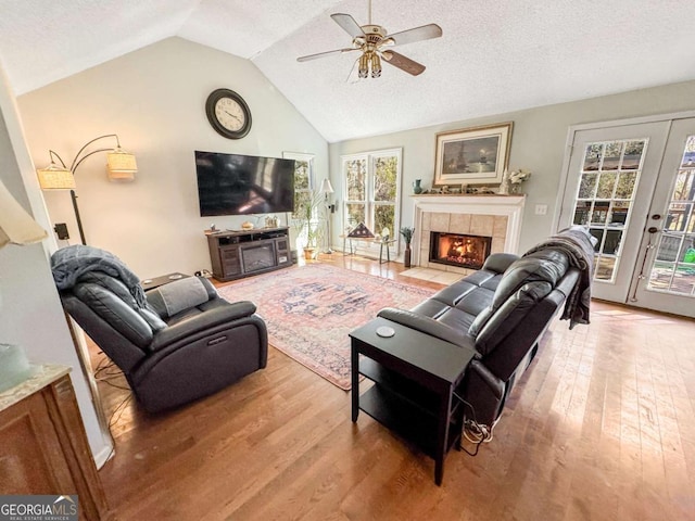 living area with light wood finished floors, a ceiling fan, vaulted ceiling, a textured ceiling, and a fireplace