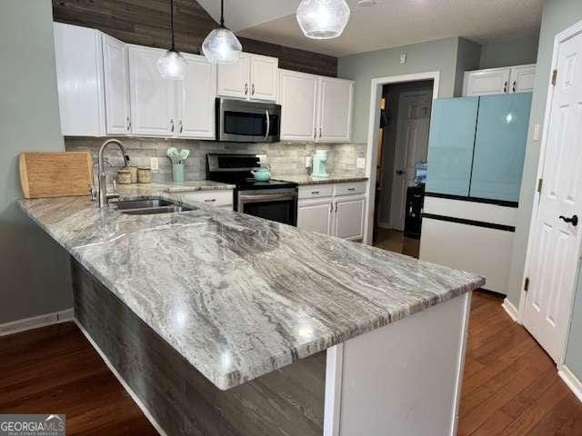 kitchen featuring a peninsula, appliances with stainless steel finishes, a sink, and white cabinetry