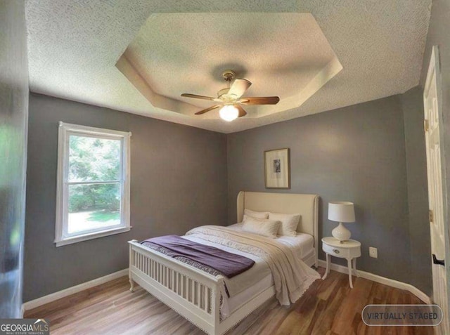 bedroom featuring a tray ceiling, a textured ceiling, baseboards, and wood finished floors