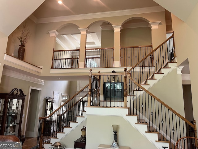 stairs featuring a towering ceiling, ornate columns, and crown molding