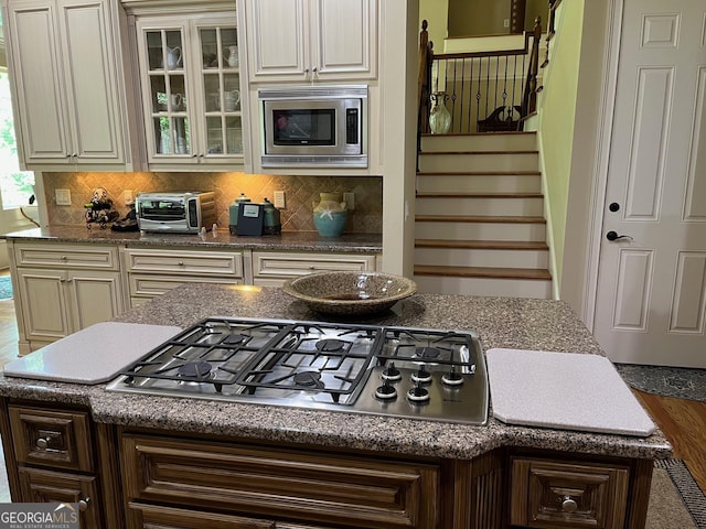 kitchen with a toaster, a kitchen island, cream cabinetry, appliances with stainless steel finishes, and glass insert cabinets