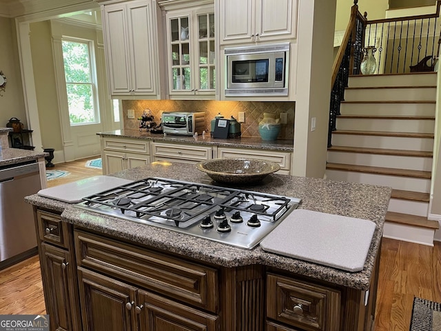 kitchen featuring dark brown cabinetry, stainless steel appliances, decorative backsplash, light wood finished floors, and glass insert cabinets