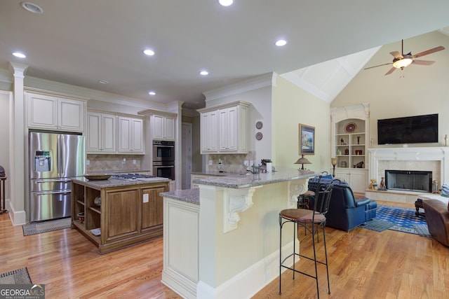 8440 Woodland Brooke Trl, Cumming, GA 30028 - kitchen featuring appliances with stainless steel finishes, open floor plan, light wood-style floors, light stone counters, and a peninsula