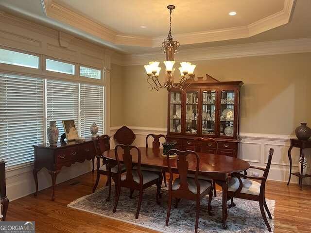 dining room with wood finished floors, a decorative wall, a raised ceiling, and an inviting chandelier