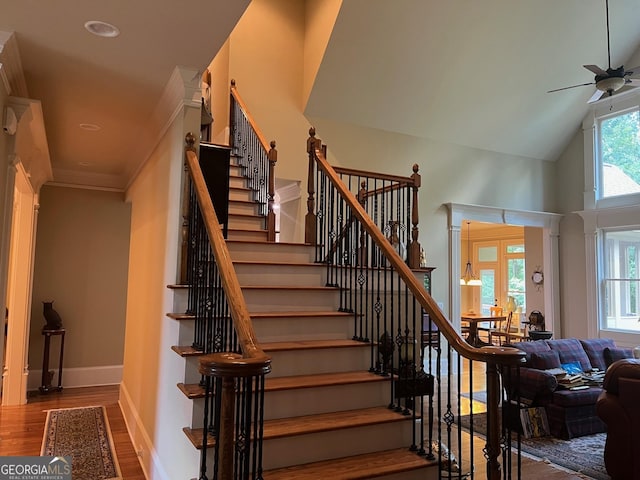 stairway with ceiling fan, high vaulted ceiling, wood finished floors, and baseboards