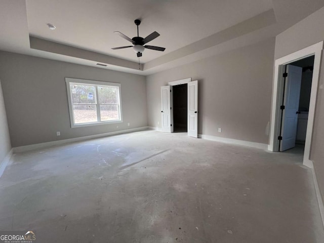 unfurnished bedroom featuring a ceiling fan, baseboards, a raised ceiling, and concrete flooring