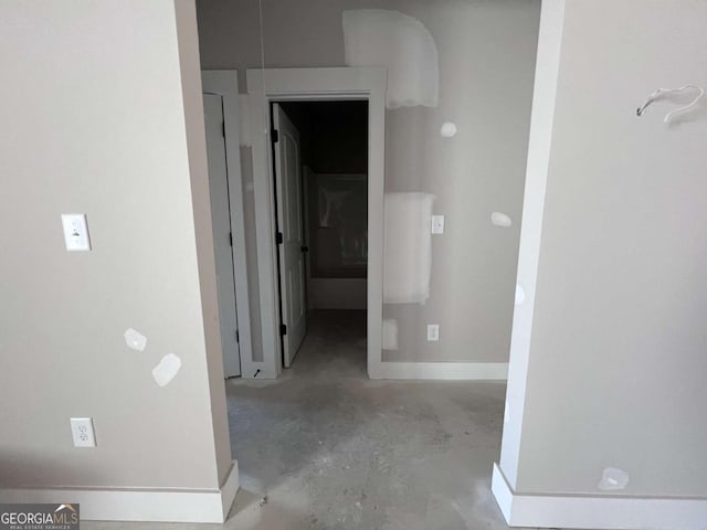 hallway featuring concrete flooring and baseboards