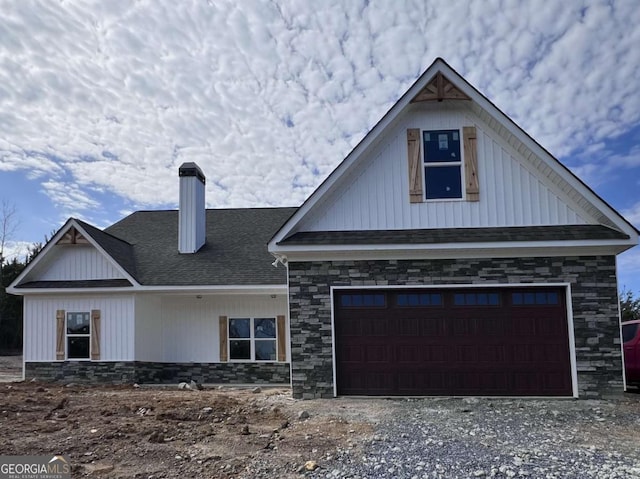 view of front of house with a garage, roof with shingles, a chimney, and gravel driveway